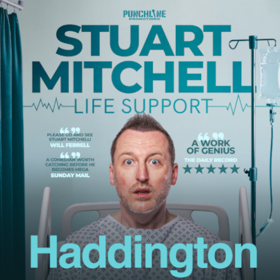 Stuart Mitchell sitting in a hospital bed with a drip behind him