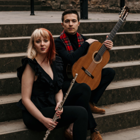 JKL Duo sitting outside on steps holding a flute and a classical guitar