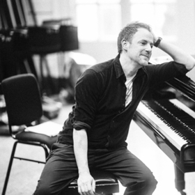 Gareth Williams seated at and leaning on a piano