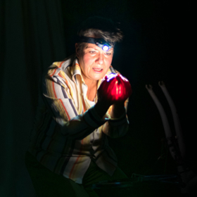 A person with a head torch on, gazes at their hands which hold a red glowing object