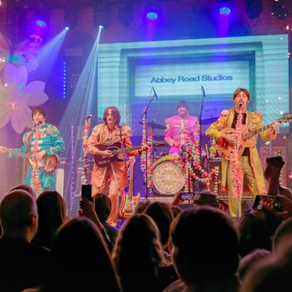 Four performers playing guitars and singing on stage, dressed in the style of The Beatles Sergeant Pepper costumes
