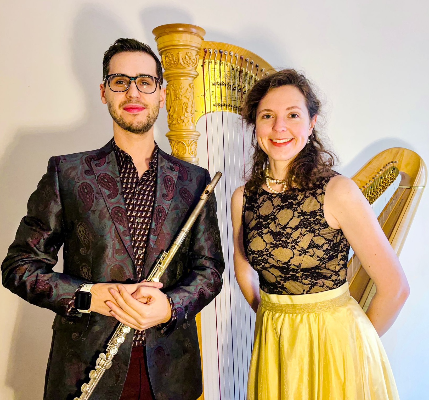 Two performers, the man holds a flute and there is a golden harp behind the woman