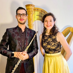Two performers, the man holds a flute and there is a golden harp behind the woman