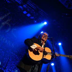 Dougie Maclean smiling holding a guitar