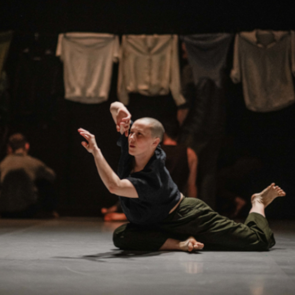 A dancer is on the floor, leaning forward with arm extended