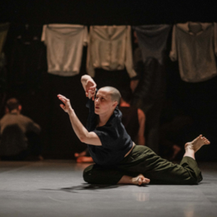 A dancer is on the floor, leaning forward with arm extended