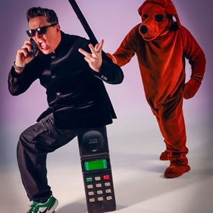A man is sat upon a comically large phone with a big red dog ready to attack him with a stick, stood behind him.